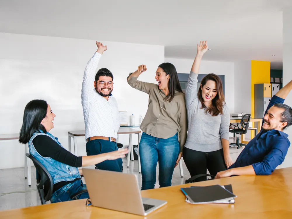 Equipo de profesionistas celebrando un logro con los brazos en alto